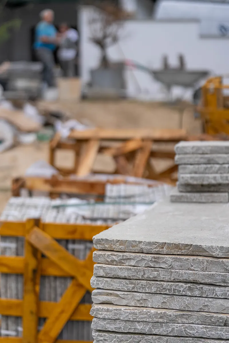 Pile de dalles Tandur aux bords éclatés au premier plan d'un chantier, palettes en arrière-plan