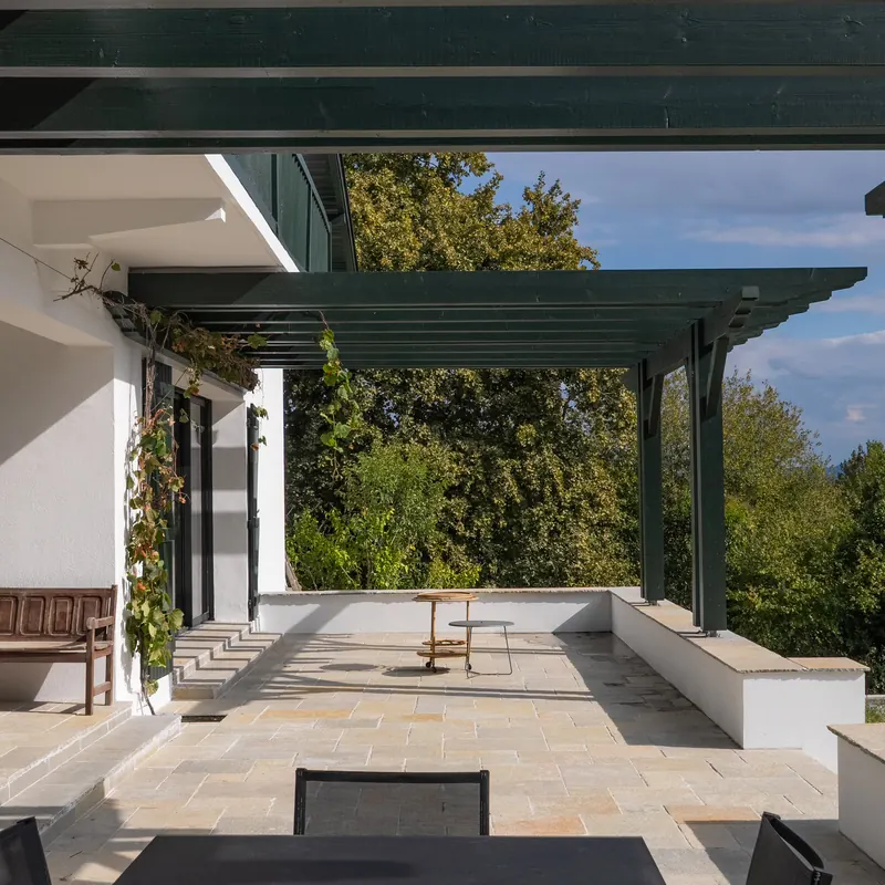 Terrasse en dallage Tandur jaune sous une pergola verte, marches et muret coiffé